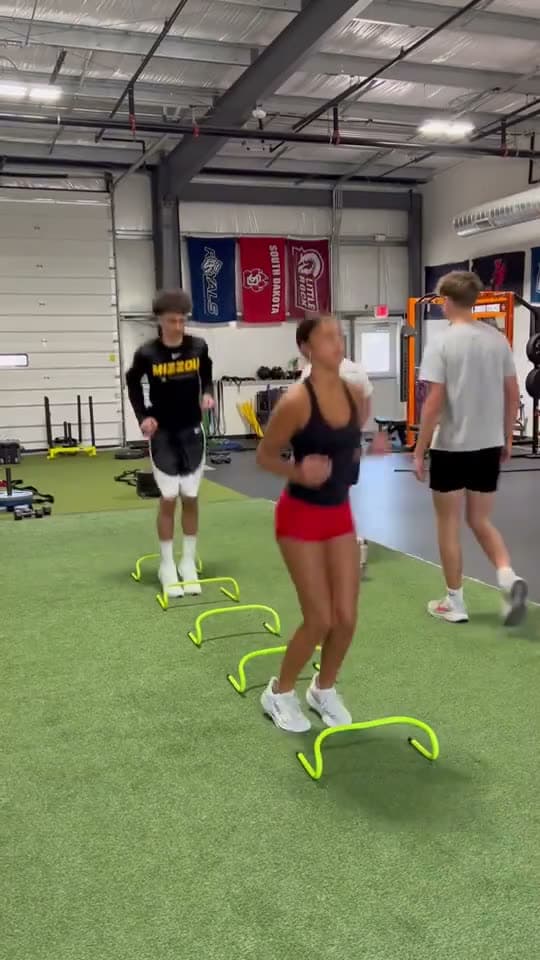 Athletes run hurdle drills on the turf.
